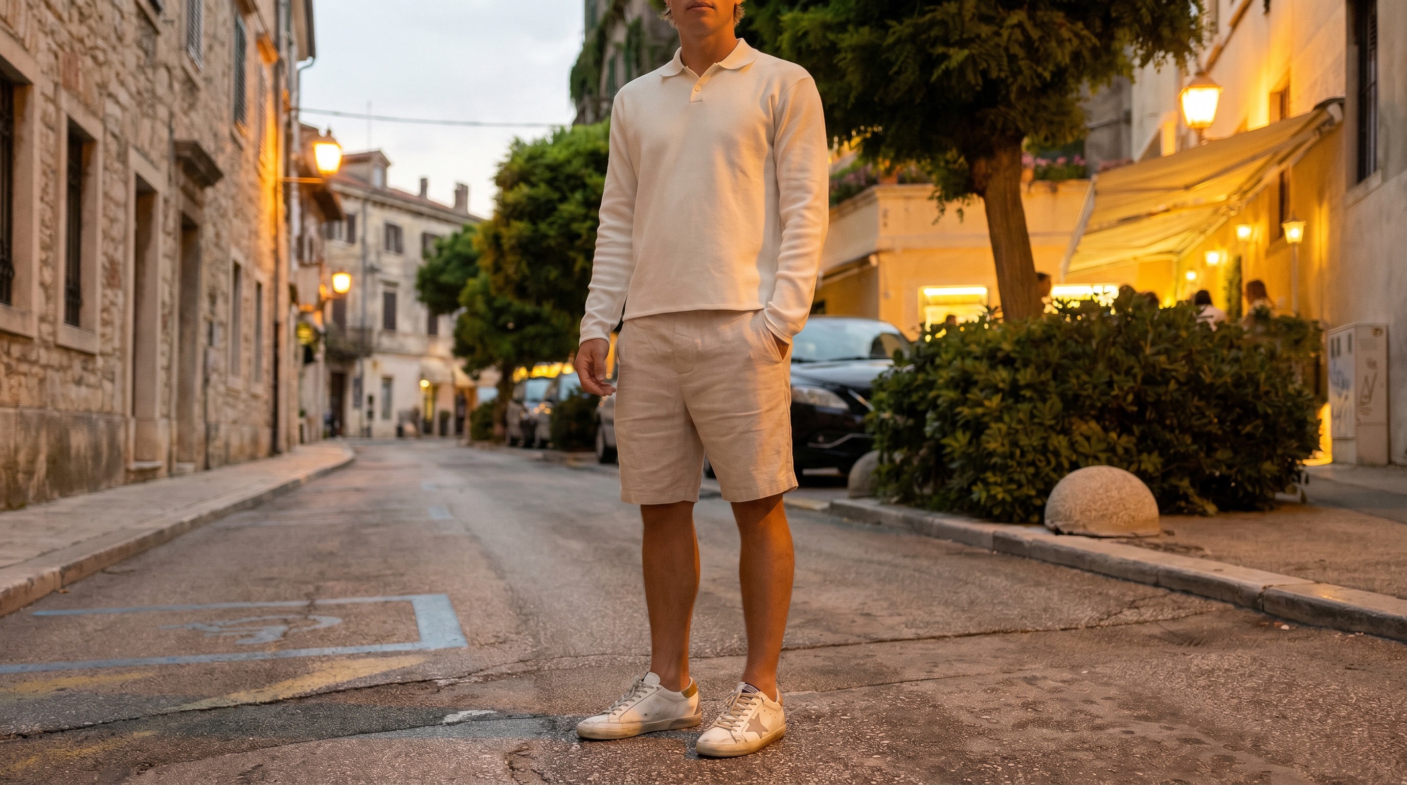 On-location photo of a model wearing a cream polo and beige shorts on a European street at dusk