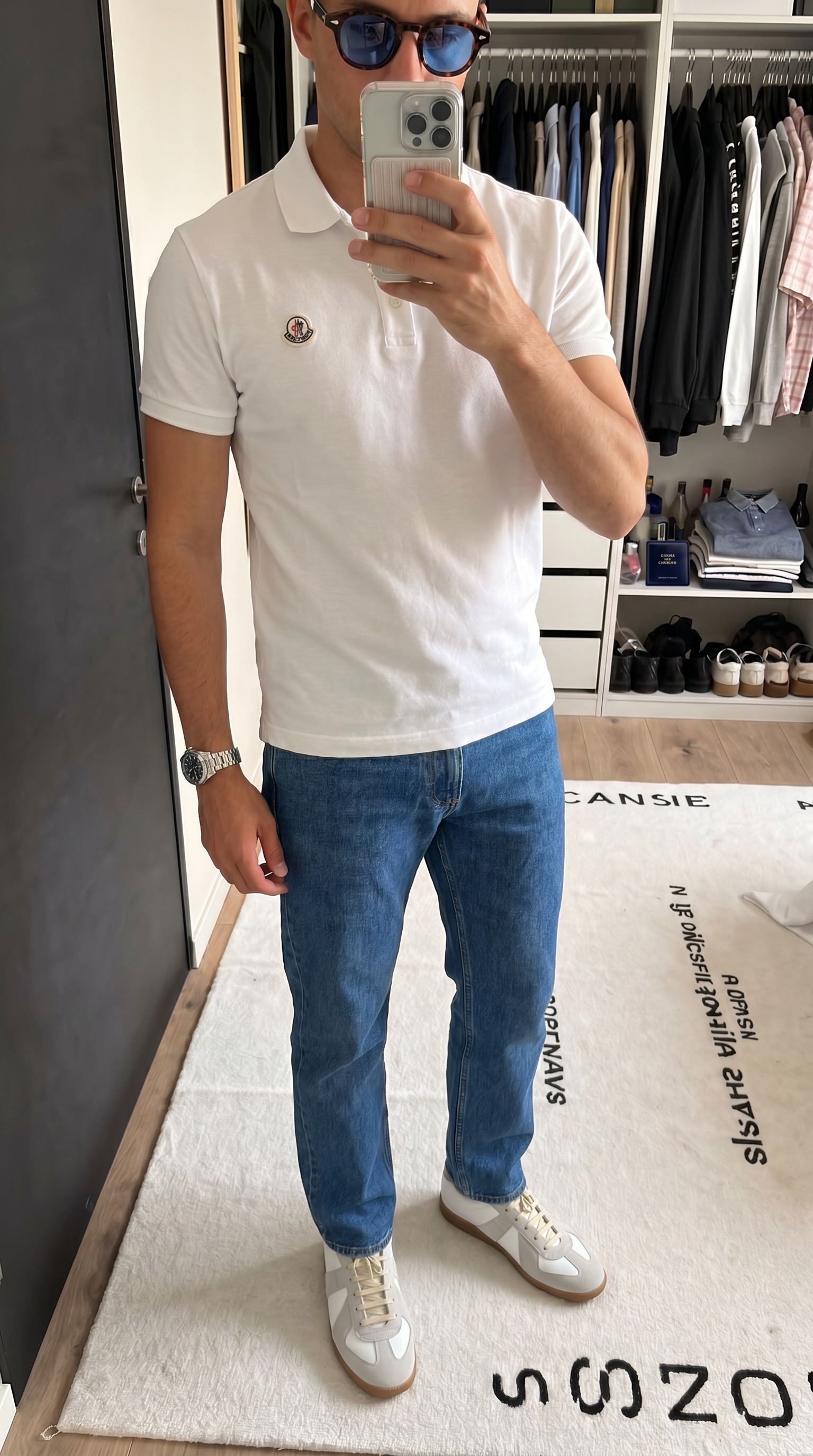 On-model mirror photo of a model wearing a white Moncler polo, jeans and sneakers