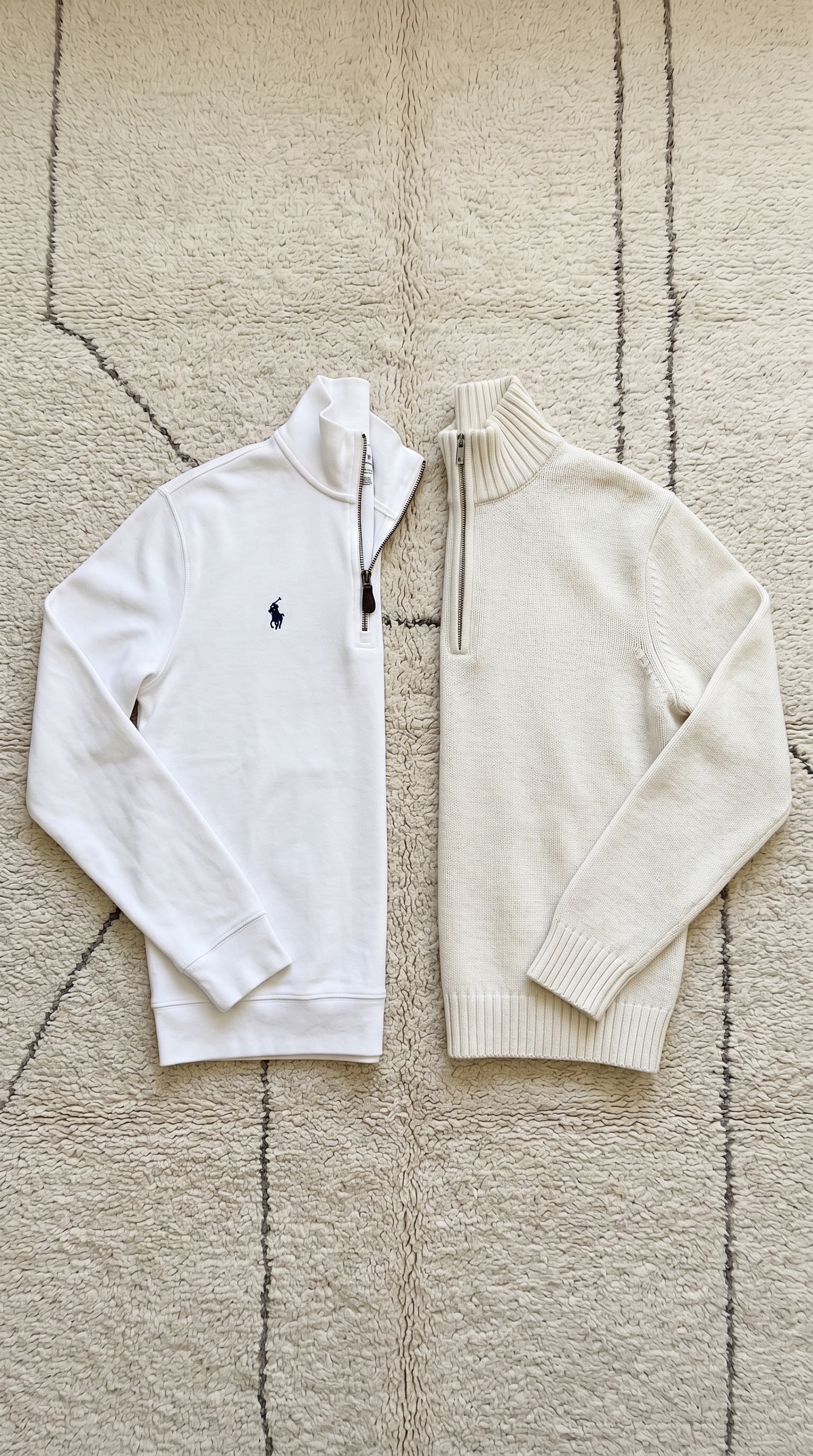 Product flat-lay of a white and a cream quarter-zip sweater side by side on a rug